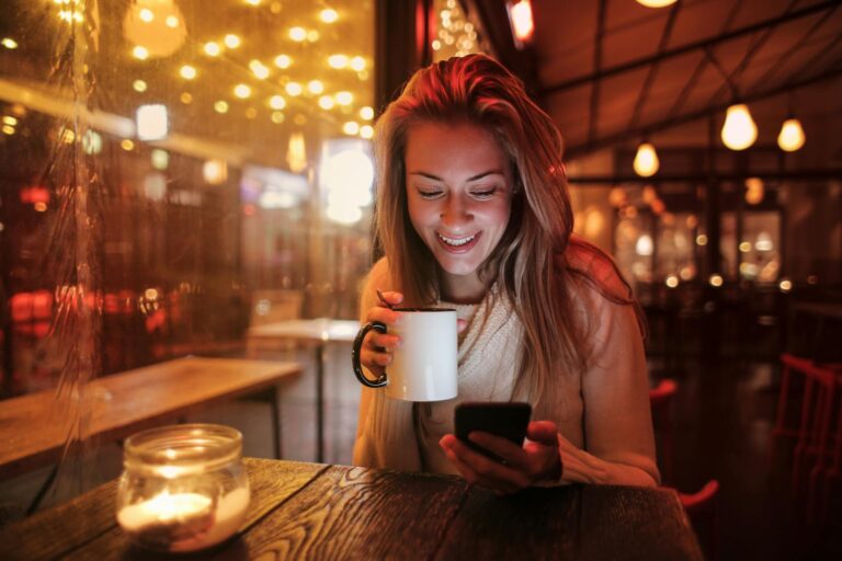 woman holding white ceramic mug looking at her cellphone