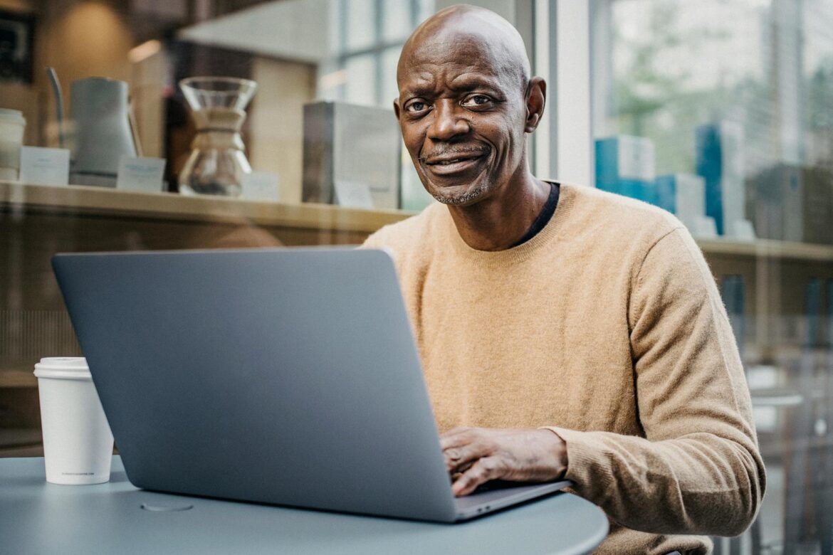 smiling middle aged black man working remotely on netbook in cafe